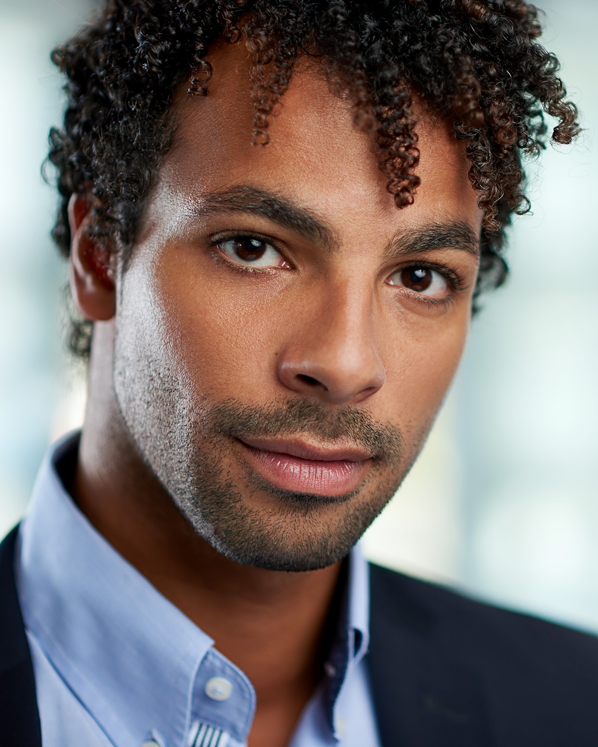 Portrait of a confident young mixed race male employee part of a business team. Serie shot with a pastel, out of focus glass window background.